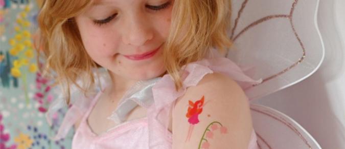 A young girl wearing fairy wings looks a temporary fairy tattoo on her shoulder