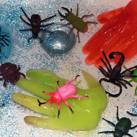 Two clear gloves are filled with coloured ice, covered in plastic creepy crawlies