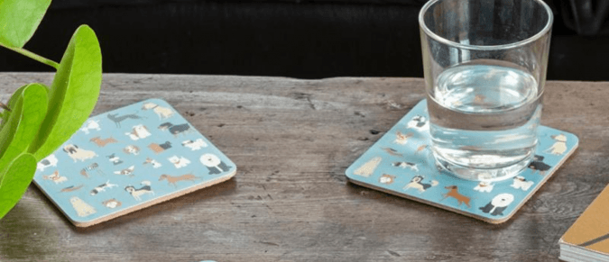 Two coasters with a dog print sit on a table with a glass of water