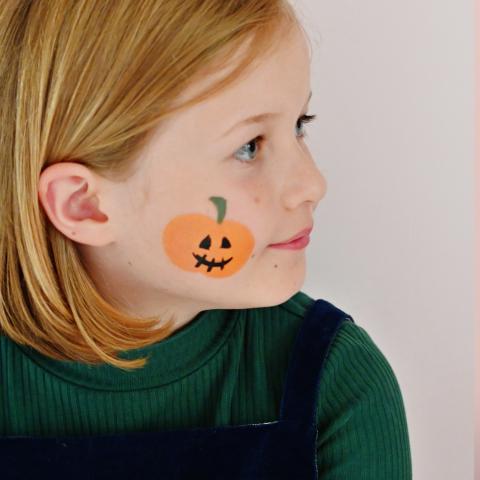 A girl has a pumpkin painted on her face